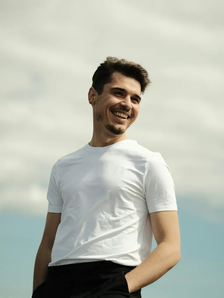 Hombre joven sonriendo al aire libre, con cielo de fondo
